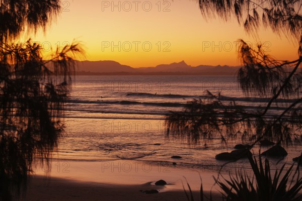 View of the ocean and Wategos Beach on the promenade at sunset. Mt- Warning, Wollumbin in the background of the red sunset on the beach