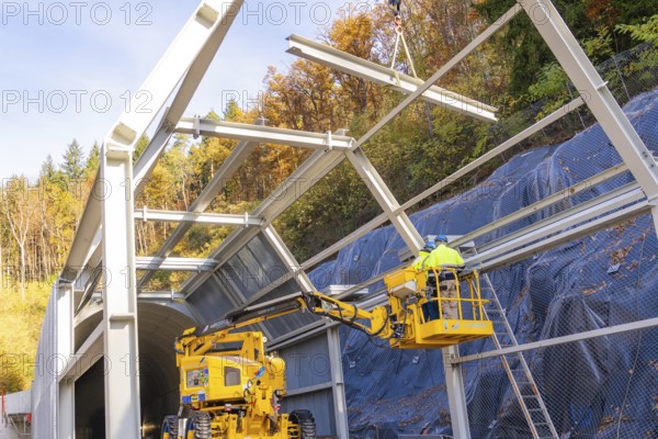 Workers on a lift building tunnel surrounded by colorful autumn trees, Hermann Hesse Railway bat tunnel construction site, Calw, Black Forest, Germany