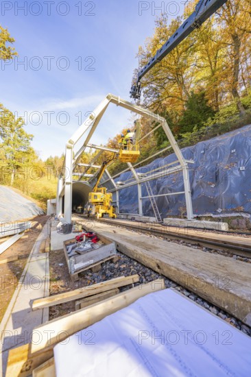 Crane lifts construction material for a tunnel surrounded by autumnal forest and blue skies, Hermann Hesse Railway Bat Tunnel construction site, Calw, Black Forest, Germany