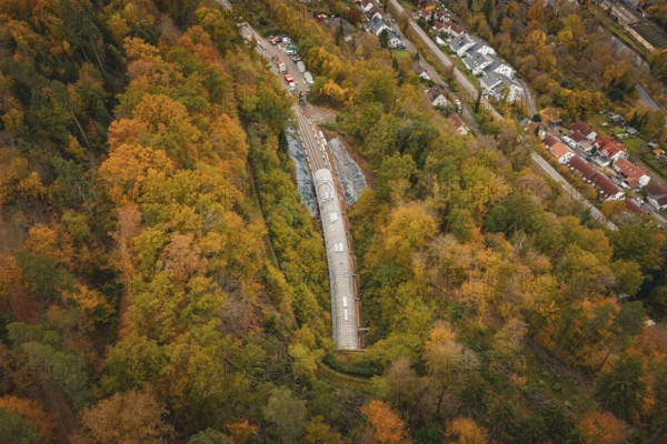 Aerial view of a railway tunnel surrounded by autumnal forest and nearby houses, Hermann Hesse Railway bat tunnel construction site, Calw, Black Forest, Germany