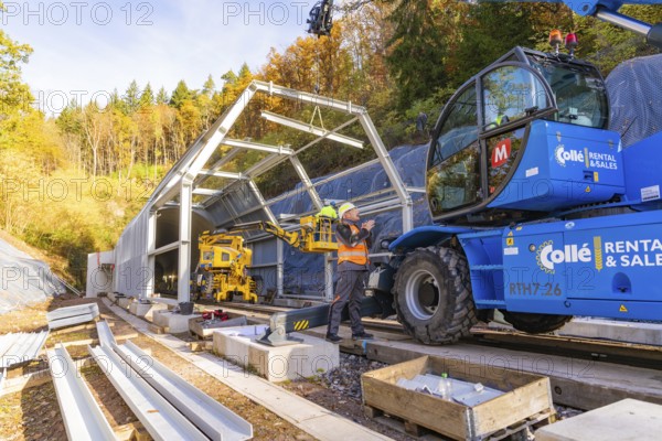Workers use cranes to build a structure along a rail line in the forest, Hermann Hesse Railway bat tunnel construction site, Calw, Black Forest, Germany