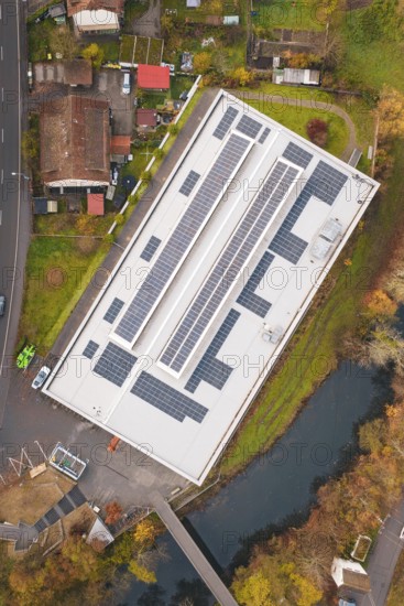 Building with solar roof, surrounded by a village and river, viewed from the air in an autumn landscape, PV at Walther Lindner Sporthalle Calw, Black Forest, Germany