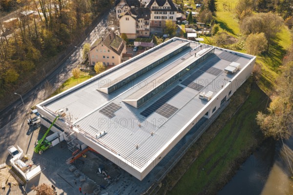 Modern building with solar panels, surrounded by a river and autumnal nature, viewed from the air, PV at Walther Lindner Sporthalle Calw, Black Forest, Germany
