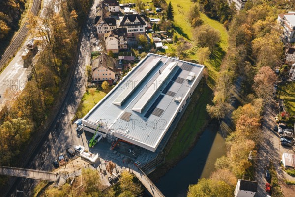 Bird's eye view of a modern building with solar cells, nestled in an autumnal village and river landscape, PV at Walther Lindner Sporthalle Calw, Black Forest, Germany