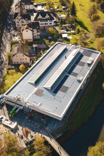 Aerial view of a modern building with solar panels on the roof, surrounded by an idyllic village and autumn landscape, PV at Walther Lindner Sporthalle Calw, Black Forest, Germany