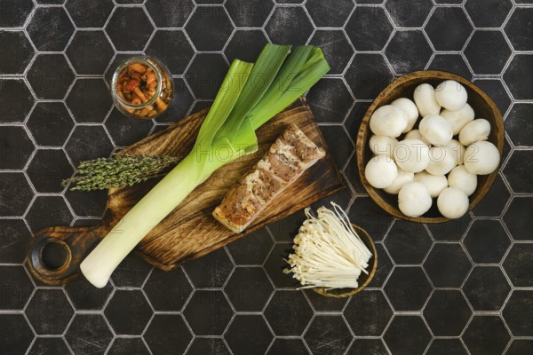 Fresh leeks, bacon and thyme on a wooden cutting board. A jar of pickled honey mushrooms and fresh enoki and champignon sit nearby, ready to enhance a delicious meal. Perfect for a home-cooked dish