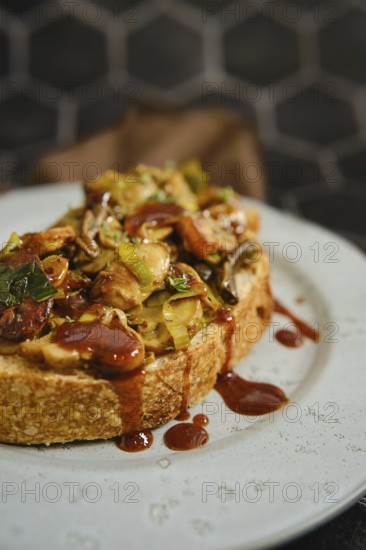 A warm mushroom sandwich is served on a rustic plate, topped with honey mushrooms, enoki mushrooms, champignon, and fresh leek