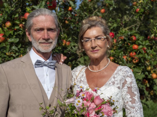 Elderly couple's wedding, look in front of a tree with lots of red apples