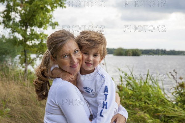 Pregnant woman with little boy at lake, mom and child hugging