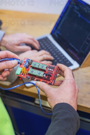 Person holding circuit board while someone is programming on a laptop, Jugend Forschungszentrum Nagold, Landkreis Calw, Germany