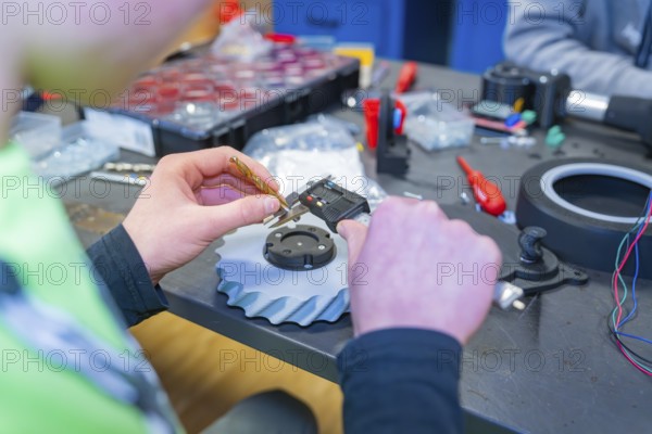 Person measuring gear at a table full of tools, Jugend Forschungszentrum Nagold, Calw district, Germany