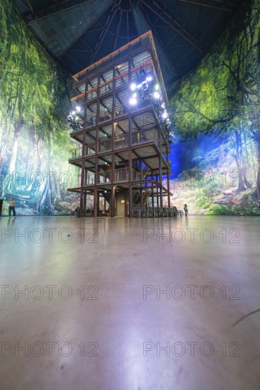 Large wooden structure in an interior surrounded by forest landscape wallpaper under a vaulted roof, Amazonia exhibition, Gasometer, Pforzheim, Germany