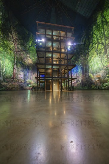An artificial jungle installation with a green illuminated wooden tower in a hall, Amazonia exhibition, Gasometer, Pforzheim, Germany
