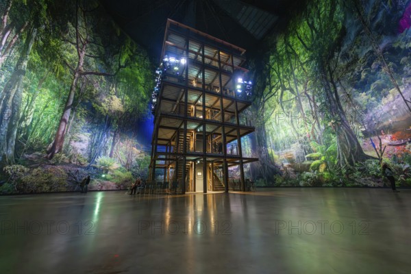 A multi-storey timber building in a glowing green artificial forest installation, Amazonia exhibition, Gasometer, Pforzheim, Germany