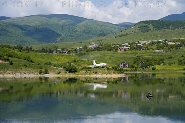 Lakeside village with mountains in the background, calm water with reflection, Tu-134A aircraft as an exhibit at Hrazdan Reservoir, Kotayk Province, Armenia