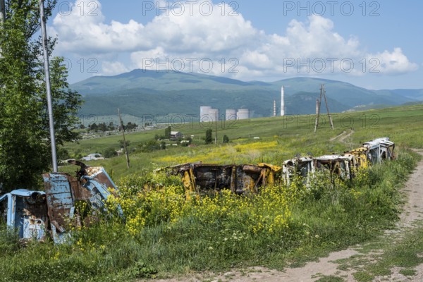 Rusty vehicles stand in a meadow in front of a wooded mountain panorama, scrap cars serve as a fence near Zovaber, Kotayk province, Armenia