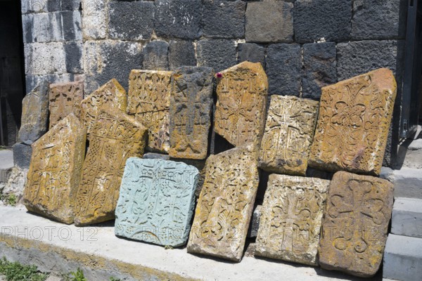 Decorated, engraved tombstones lean against an old wall, cross stones at Sevanavank Monastery, Sevan Monastery, Gegharkunik Province, Armenia