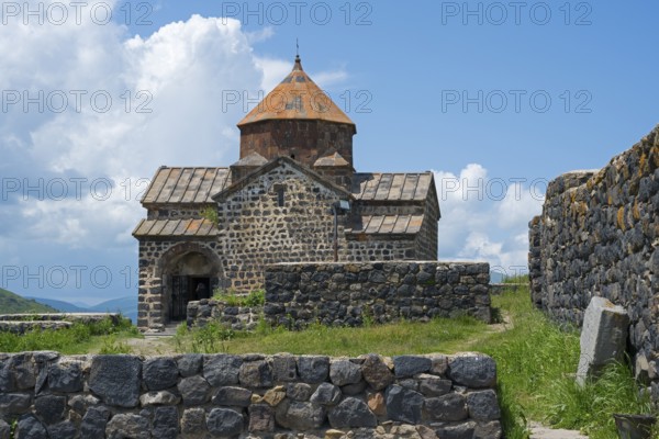 Front view of a historic stone church with brick wall and overgrown landscape, Sevanavank Monastery, Gegharkunik Province, Armenia