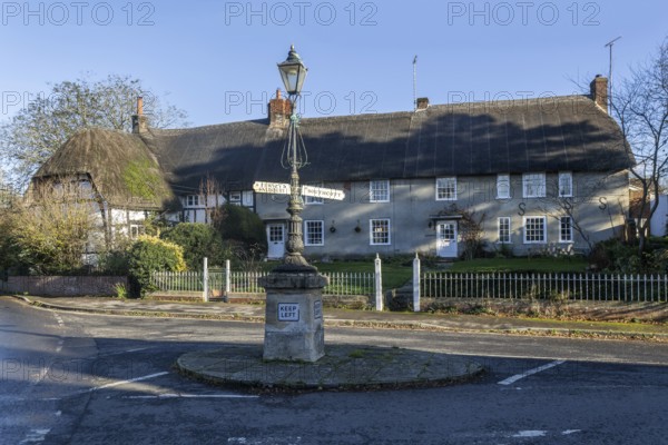 Historic signpost with direction arrows, thatched cottages in village of Pewsey, Wiltshire, England, UK