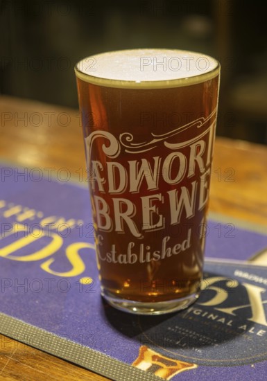 Full pint glass of Wadworth 6X real ale beer on pub bar mat, Wiltshire, England, UK