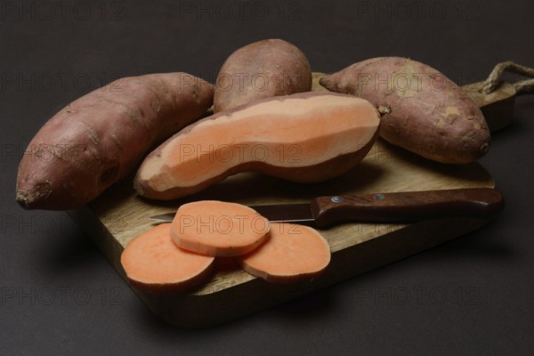 Sweet potatoes with kitchen knife on wooden board, Ipomoea batatas