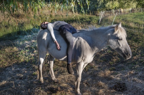 Young girl lying on her white mare in the pasture, Othenstorf, Mecklenburg-Western Pomerania, Germany