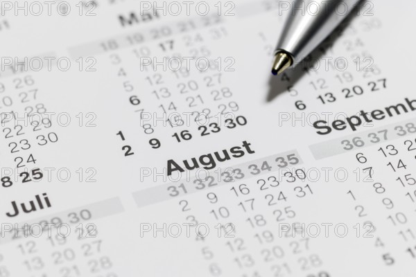 Close-up of a calendar with ballpoint pen pointing to the month of August