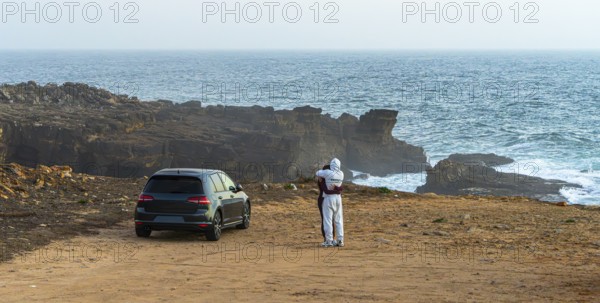 Young couple in love standing on the coast of Farol de Cabo Raso lighthouse, SÃ£o Bras de Sanxete fortress, Cascais, Portugal