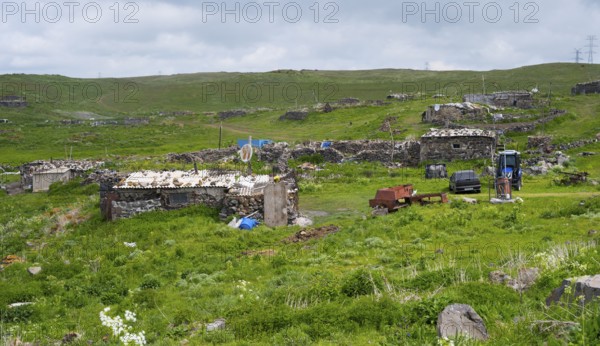 Rural town with dilapidated buildings and green fields under cloudy sky, small town on the M10 near Nshkhark, Gegharkunik province, Armenia