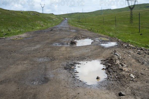 Unpaved road with potholes surrounded by green hills and power lines, M10 near Geghovit, Gegharkunik Province, Armenia