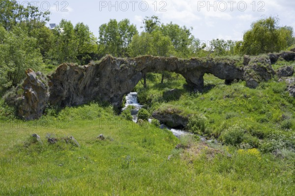 Scene with a natural rock arch and a small waterfall in green surroundings, Tsakkar Bridge in the village of Tsakkar, Gegharkunik Province, Armenia