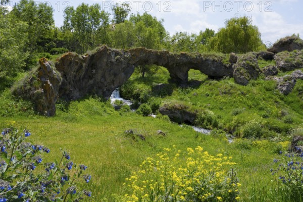Landscape with natural rock arch, green vegetation and flowing stream, Tsakkar bridge in the village of Tsakkar, Gegharkunik province, Armenia