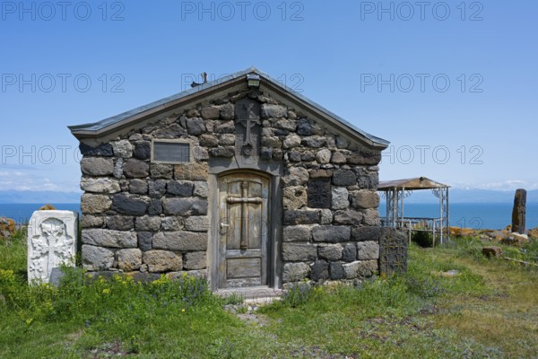 Stone chapel with wooden door in the foreground, sea in the background under clear sky, Chapel of the Holy Cross, Sarukhan, Lake Sevan, Gegharkunik Province, Armenia