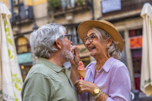 Happy senior couple enjoying a sweet treat together, with the woman playfully feeding her husband ice cream, showing their loving bond while traveling