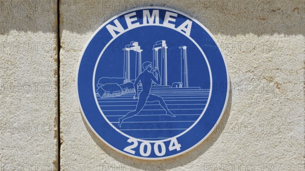 Blue sign with ancient columns and a runner in front of a stone wall, Ancient Stadium, Nemea, Peloponnese, Greece
