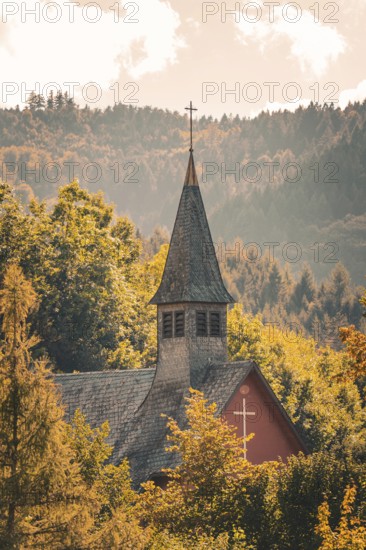 A church tower stands out picturesquely against wooded hills, surrounded by autumn colors