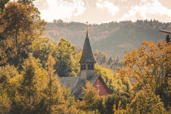 An idyllic church nestled in autumn leaves in front of a mountain landscape