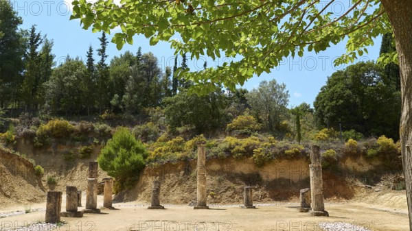 Ancient ruins with multiple pillars nestled in a lush green landscape under cloudy sky, Ancient Stadium, Nemea, Peloponnese, Greece