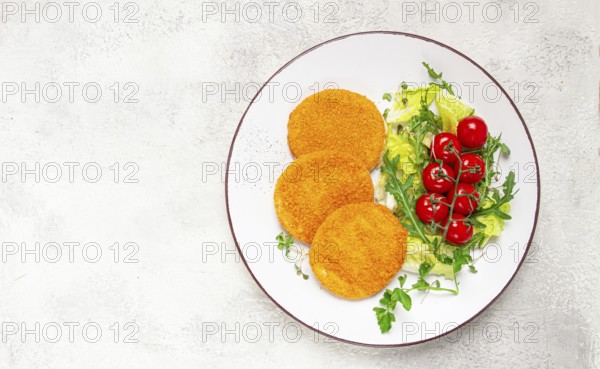 Crispy fried fish cutlets, fish burgers, on a white plate, with fresh lettuce leaves, arugula and cherry tomatoes, homemade, no people