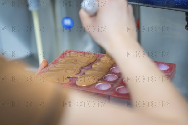 Person fills chocolate into red chocolate molds with a ladle, Christmas baking, Haselstaller Hof, Wildberg, Calw district, Germany