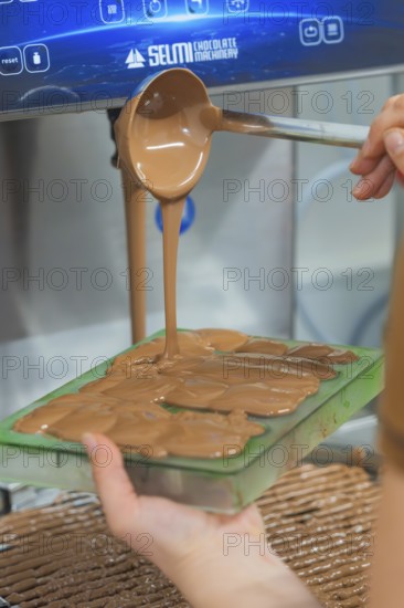 Hand pouring warm chocolate from a ladle into chocolate molds, Christmas baking, Haselstaller Hof, Wildberg, Calw district, Germany