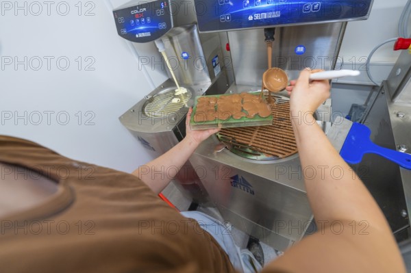 Person pouring liquid chocolate into a green mold next to a chocolate tempering machine, Christmas baking, Haselstaller Hof, Wildberg, Calw district, Germany