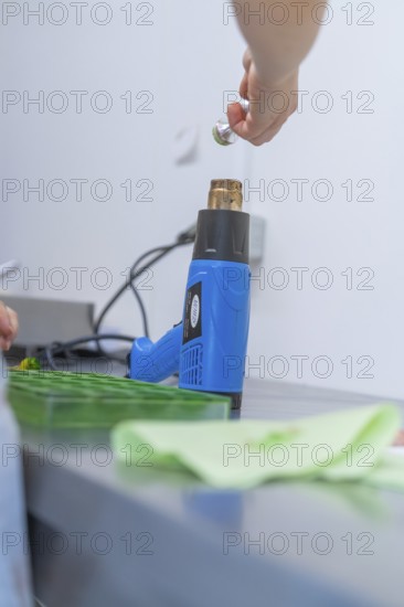 Person uses a blue heat gun to process green objects on a workbench, Weihnachtsbacken, Haselstaller Hof, Wildberg, Calw district, Germany