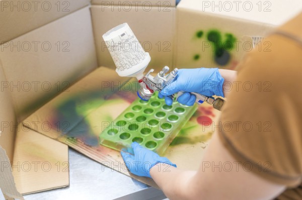 Person spraying green paint into a mold on a craft table surrounded by cardboard, Christmas baking, Haselstaller Hof, Wildberg, Calw district, Germany