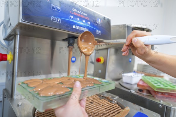 Chocolate filling is poured into molds from a tempering machine, Christmas baking, Haselstaller Hof, Wildberg, Calw district, Germany