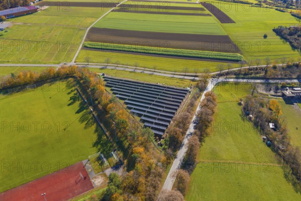 Drone shot of a solar system next to a sports field, surrounded by colorful autumn trees, Bau PV Freifaechenanlage, Weil der Stadt, Germany