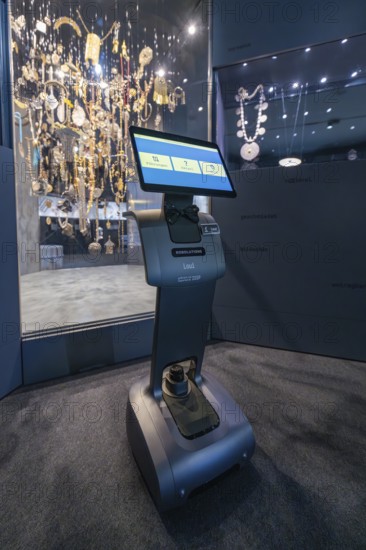A robot in front of a glass display case full of jewelry in a dark exhibition area, robotic personality Roboloutions in the jewelry museum, Pforzheim, Germany