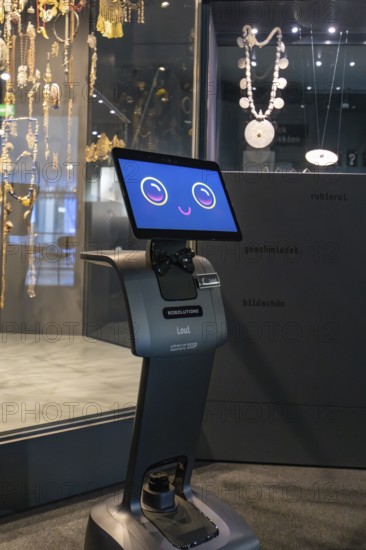 Robot with smiling display stands in front of a jewelry exhibition in the museum, robot personality Roboloutions in the jewelry museum, Pforzheim, Germany