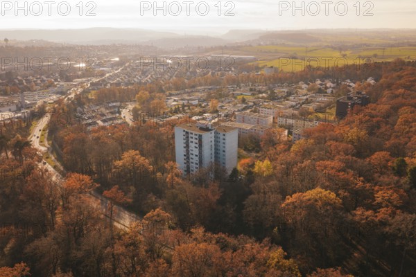 A residential building towers over an autumnal forest with a town behind it, MÃ¼hlacker, Enzkreis, Germany