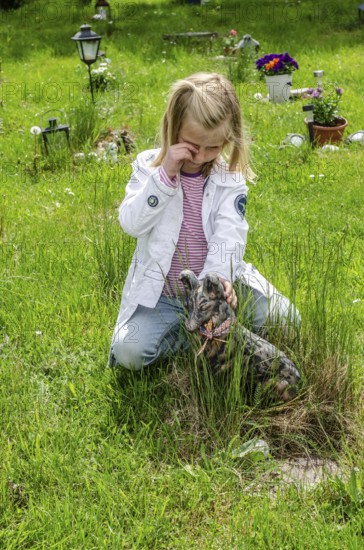 Grieving blonde 7-year-old girl at her dog's grave at pet cemetery in Ystad, SkÃ¥ne County, Sweden, Scandinavia